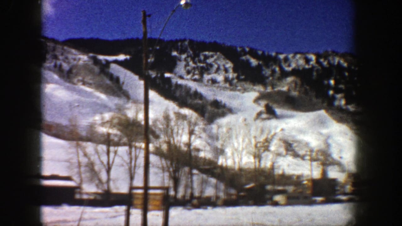 1961 Aspen, Colorado home-movie view of a snow-covered mountain slope with bare trees, utility poles, and low buildings below.