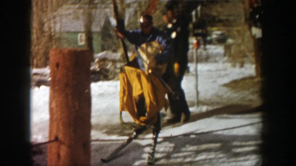 At an Aspen ski lift station, a blue-jacketed worker appears to guide a yellow carrier beside snow, trees, and lift hardware.