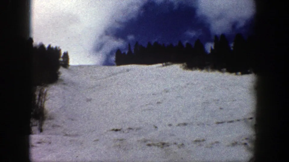 1961 Aspen home-movie frame showing a snowy mountain slope, evergreen trees, and deep blue sky with visible 8mm gate edges.