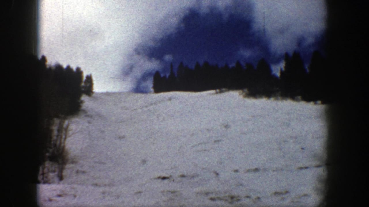 Snowy hillside with evergreen trees silhouetted against a blue and white sky.