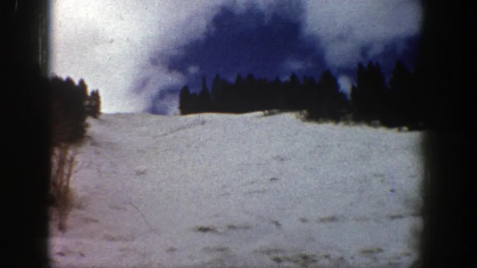 Aspen 1961 8mm frame showing a broad snowfield, silhouetted evergreens, blue sky, and slight color fading.