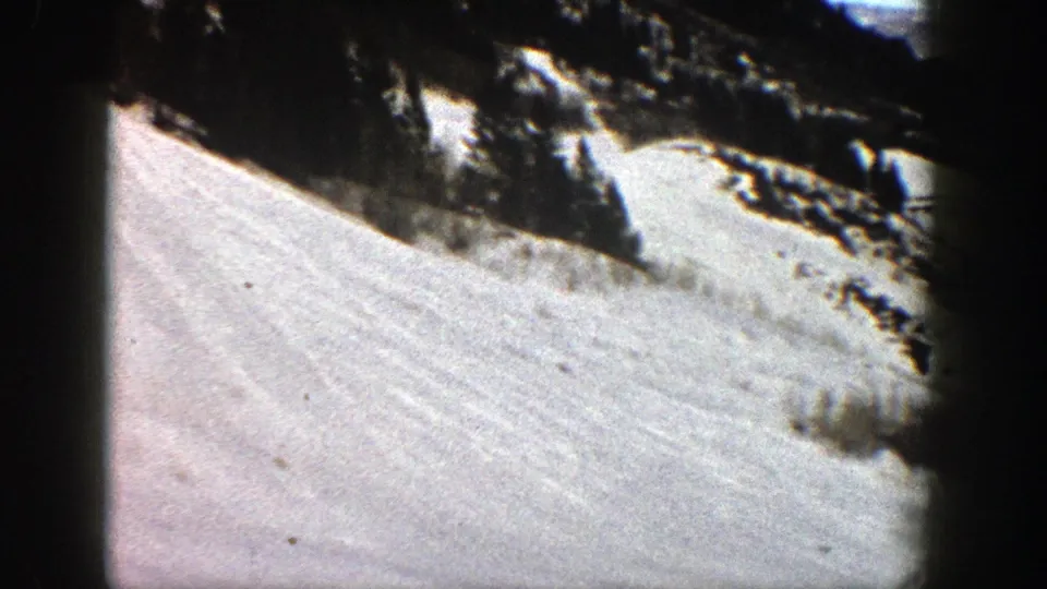 Final frame of the 1961 Aspen 8mm view, showing a broad snow-covered slope bordered by evergreens and rock.