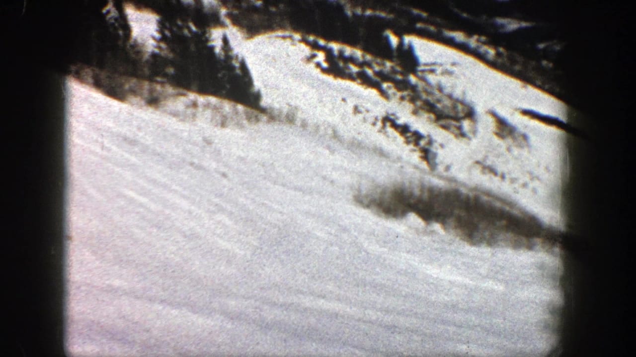 1961 Aspen home-movie frame showing a bright snowy slope below a dark mountain ridge and visible 8mm frame edges.