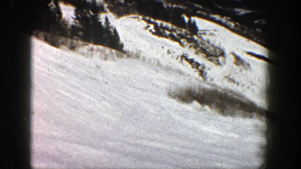 1961 Aspen home-movie frame showing a bright snowy slope below a dark mountain ridge and visible 8mm frame edges.