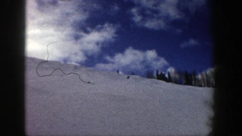 1961 Aspen ski-slope view with distant skiers crossing a white hillside beneath blue sky and scattered clouds.