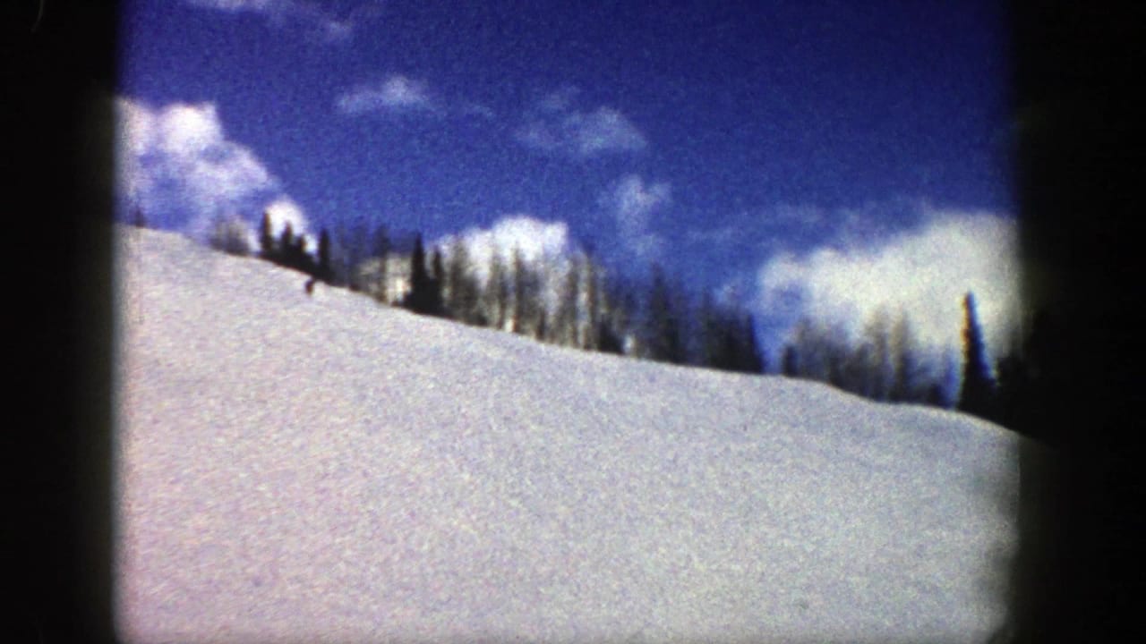 Snowy hillside below a blue sky with scattered clouds and a line of dark trees.