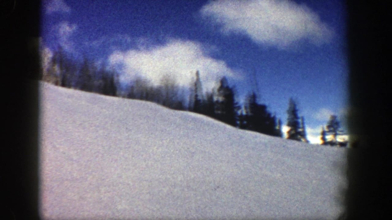 Wide snowy slope with a tree line beneath a blue sky and bright clouds.