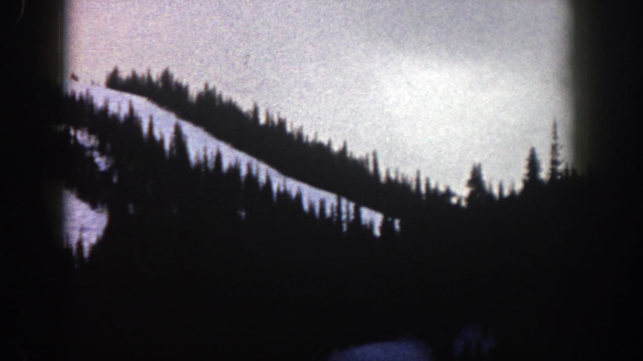 1961 Aspen-area 8mm frame showing a snow-covered slope edged by silhouetted fir trees beneath an overcast sky.