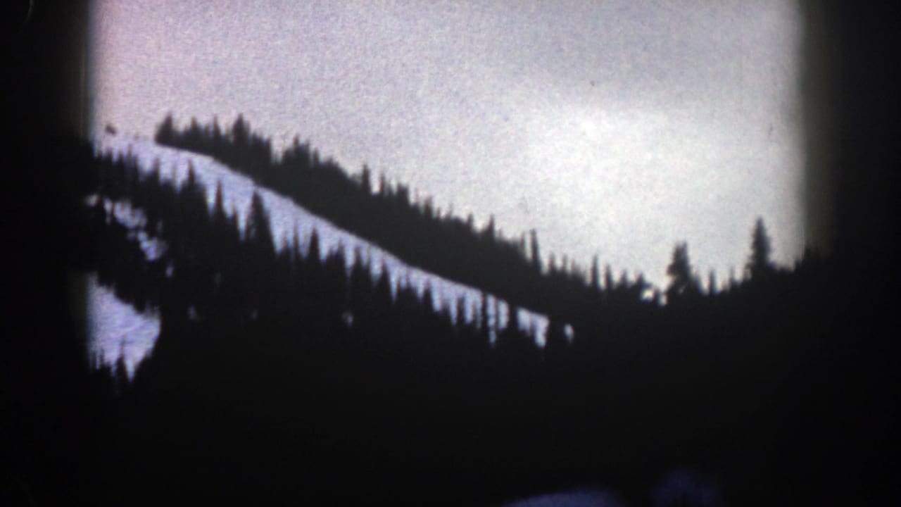 Fir-lined snowy ridge seen through rounded dark film edges.