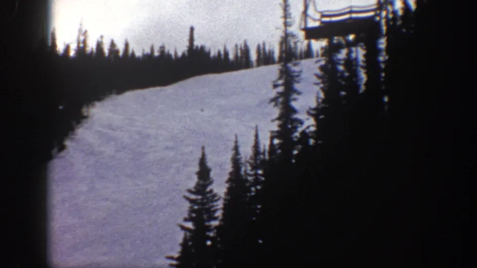 Aspen, Colorado 1961 frame showing a snowy ski slope, conifers, and a ski lift structure near the top right of the frame.