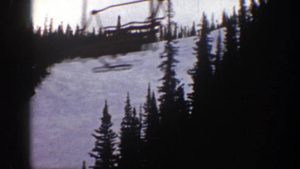 1961 Aspen, Colorado 8mm frame showing a snow-covered ski run, dark conifers, and a chairlift structure near the top of the slope.