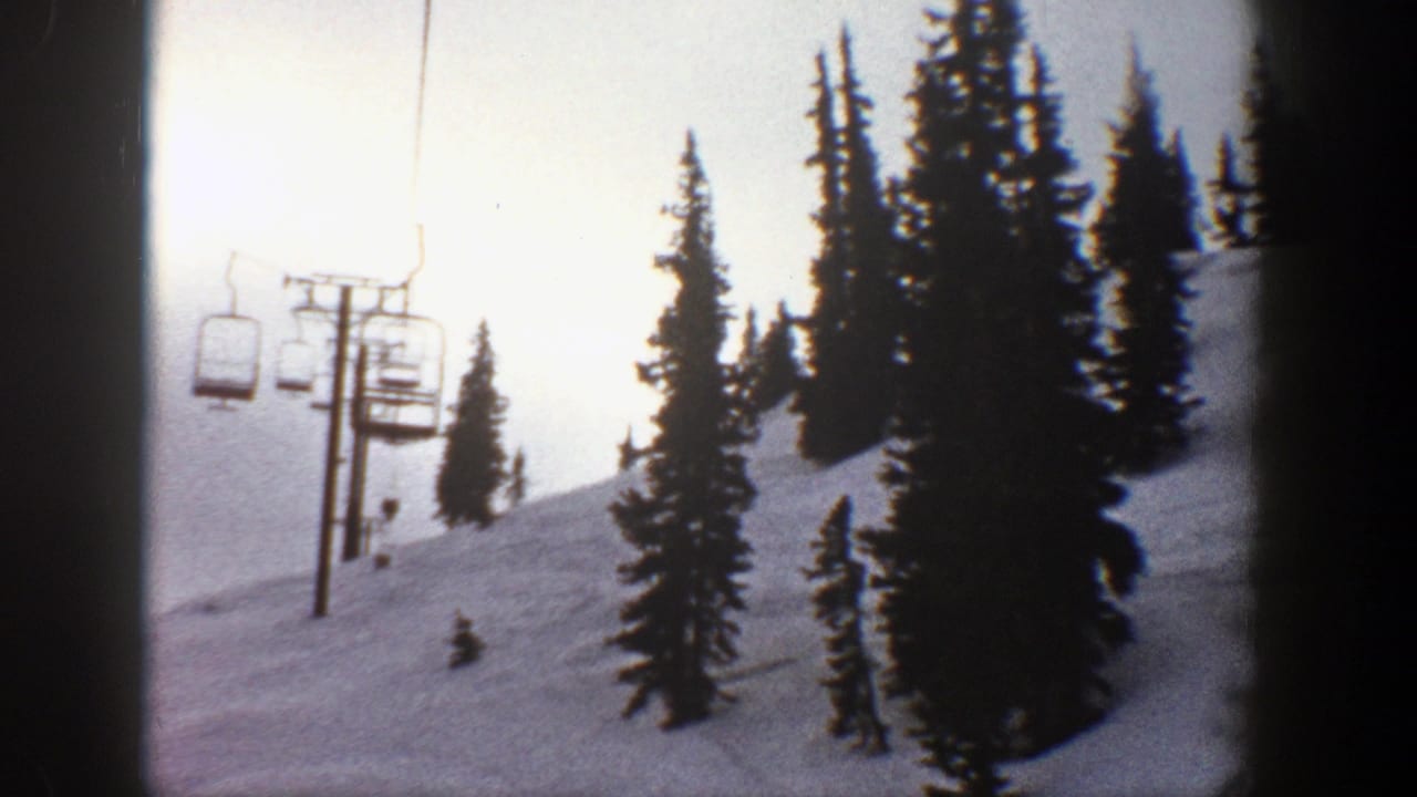 Chairlift towers and empty chairs rise along a snowy slope between tall evergreens.