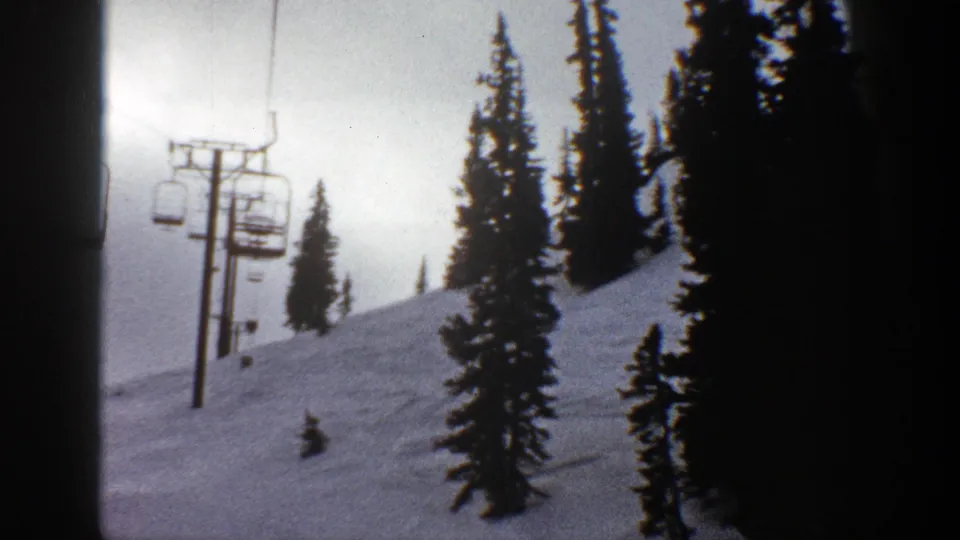 1961 Aspen, Colorado 8mm frame of a chairlift beside a quiet snow-covered ski run, with conifers silhouetted against a pale sky.