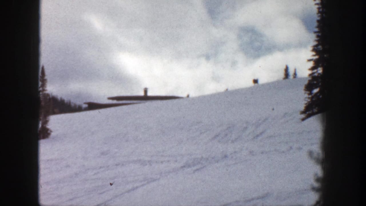 Snowy ridge with a low building in the distance and dark film border at center.