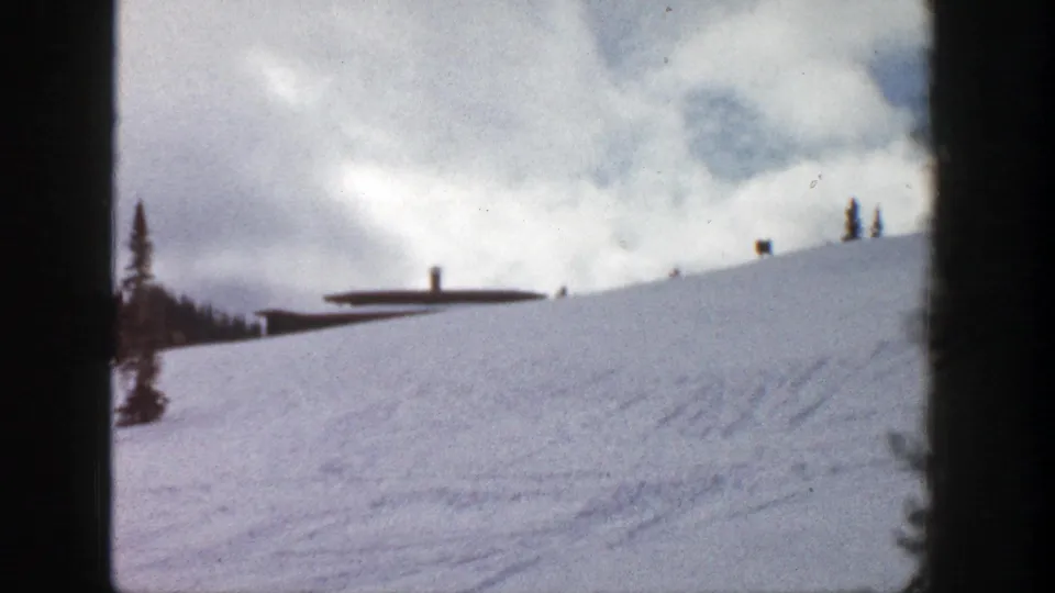 1961 Aspen home-movie view of a broad snowy hillside, distant building, ridge line, conifers, and visible 8mm frame edge.