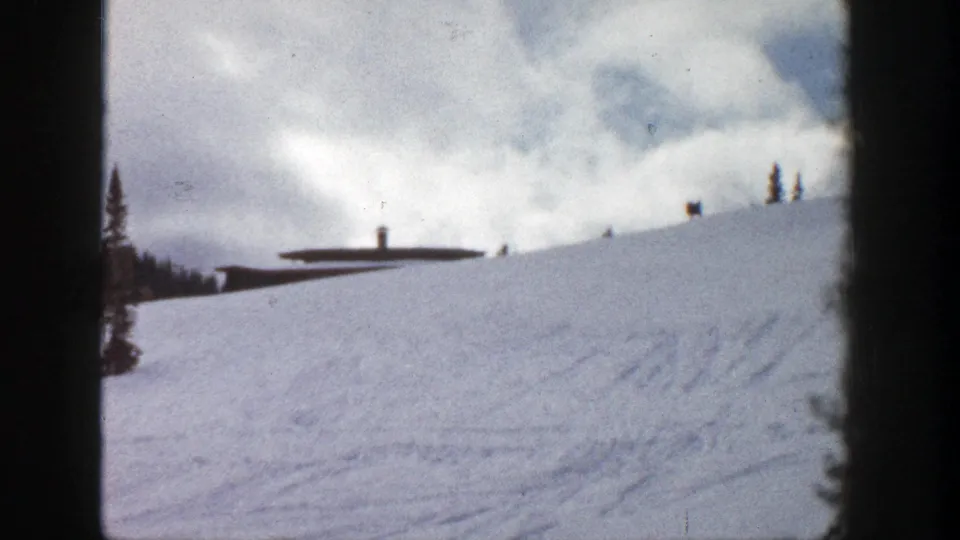 Final 1961 Aspen frame showing the snowfield, ridge-top building, sparse conifers, overcast sky, and dark vertical film border.
