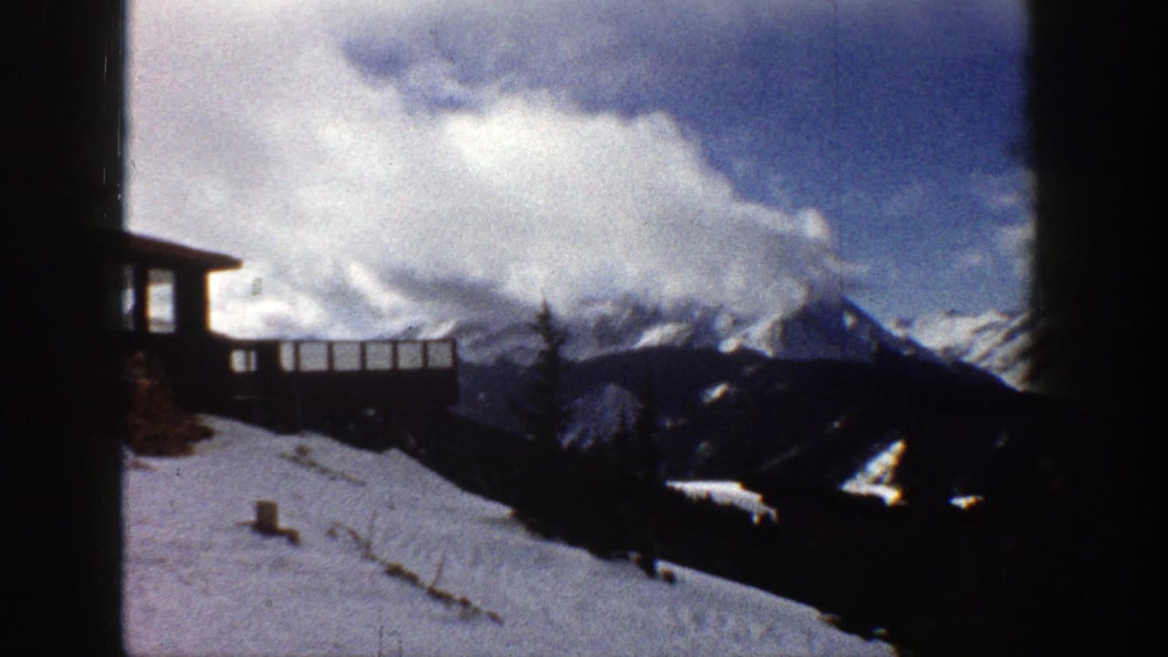1961 Aspen, Colorado 8mm frame showing a snow-covered ridge, wooden structure, evergreens, and clouded mountain peaks.