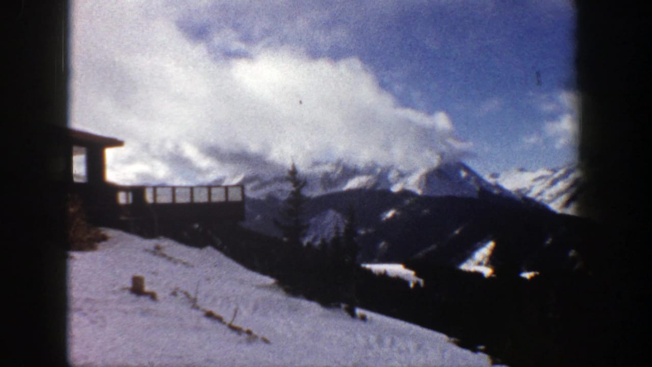 Snowy overlook with timber railing, evergreen trees, and mountain peaks in the distance.