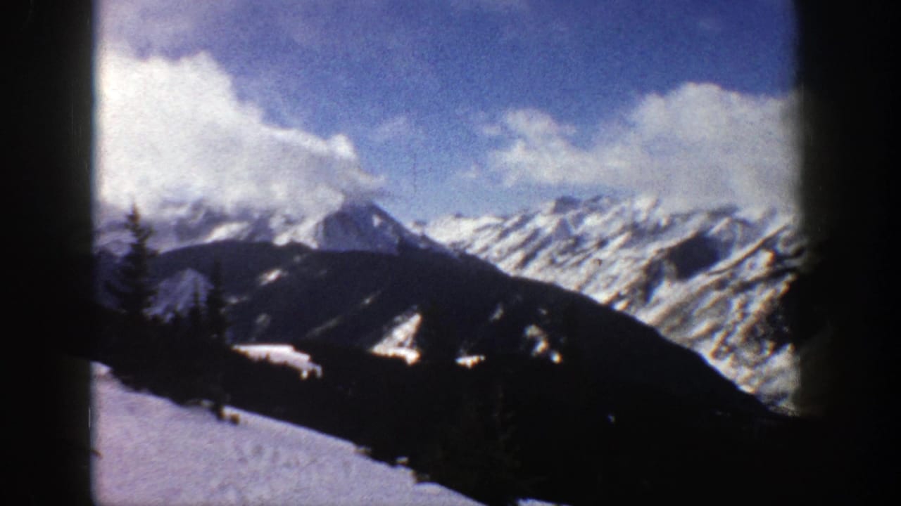 Snow-covered mountain range beneath a bright blue sky and large white clouds.