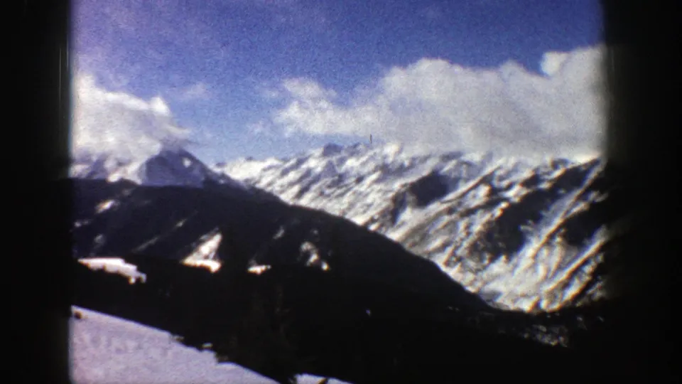 1961 Aspen, Colorado 8mm frame from a panning view across snow-striped mountains and a cloudy blue sky.