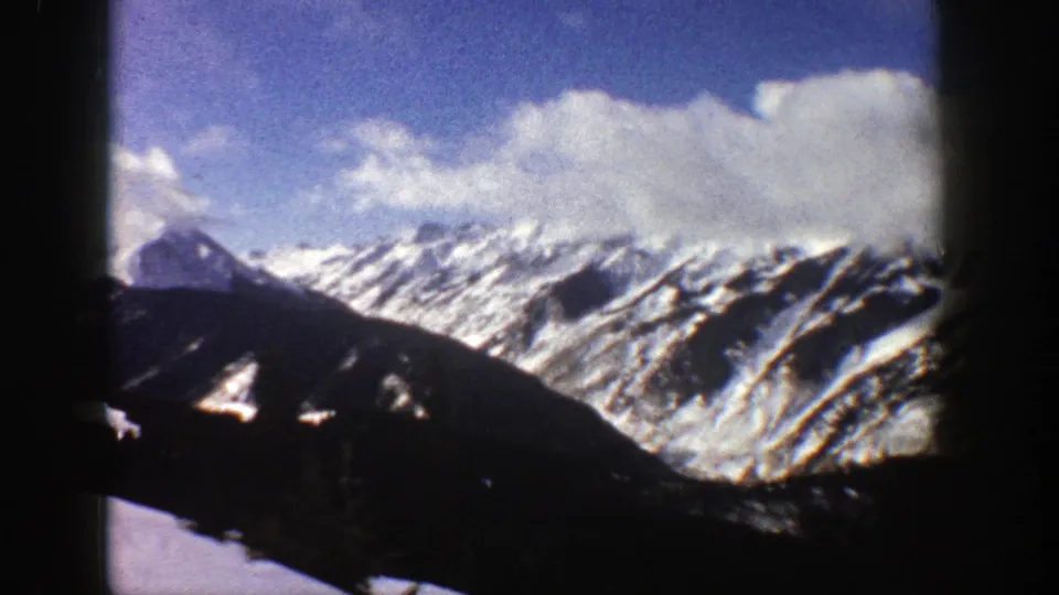 1961 Aspen, Colorado 8mm frame showing a broad snowy ridge, cloud cover, blue sky, and dark lower mountain slopes.