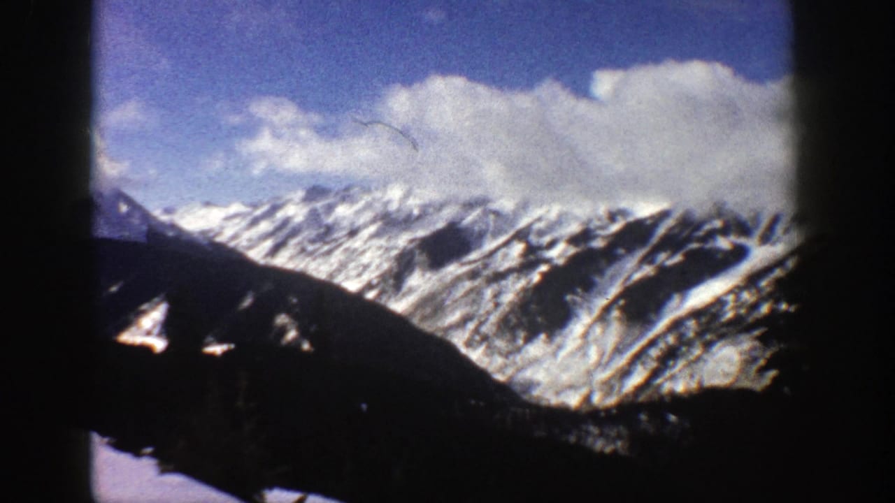Snow-covered Rocky Mountain ridges under blue sky with dark foreground slopes.