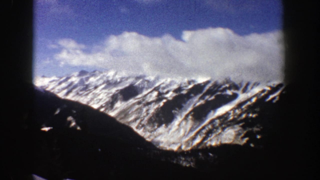 Snowy mountain range with clouds and a dark slope crossing the foreground.