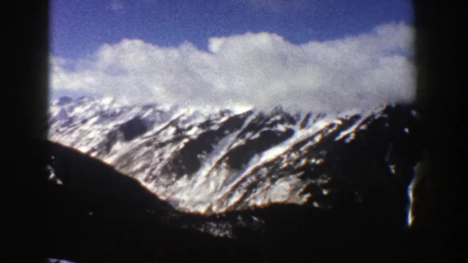 1961 Aspen-area home-movie frame with snow-capped ridges, deep shadows, blue sky, and visible 8mm contact-sheet borders.