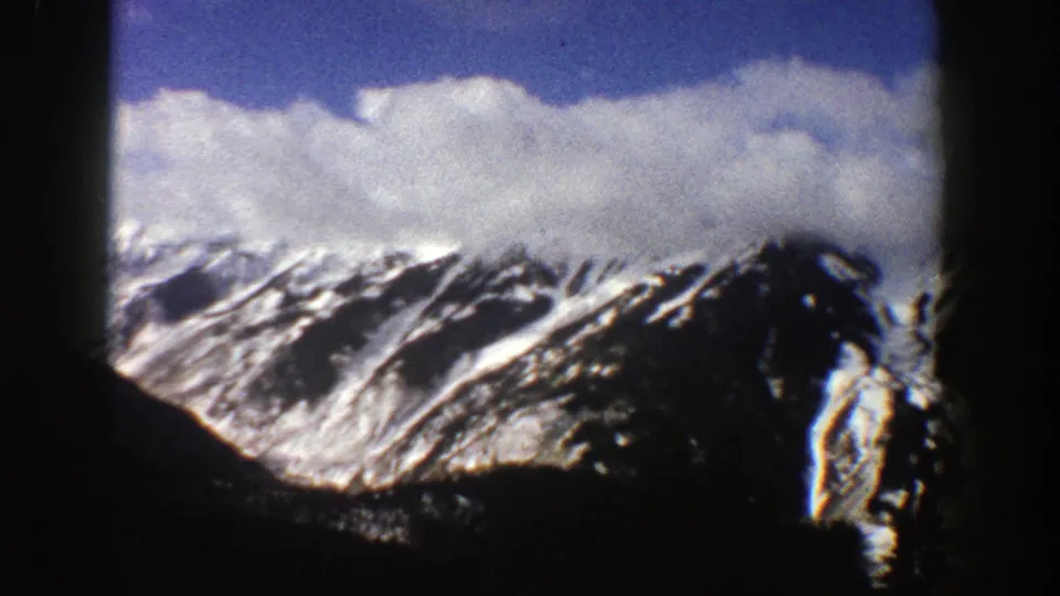 1961 Aspen-area 8mm frame showing a snow-covered Rocky Mountain ridge, cloud bank, dark foreground, and rounded film edge.