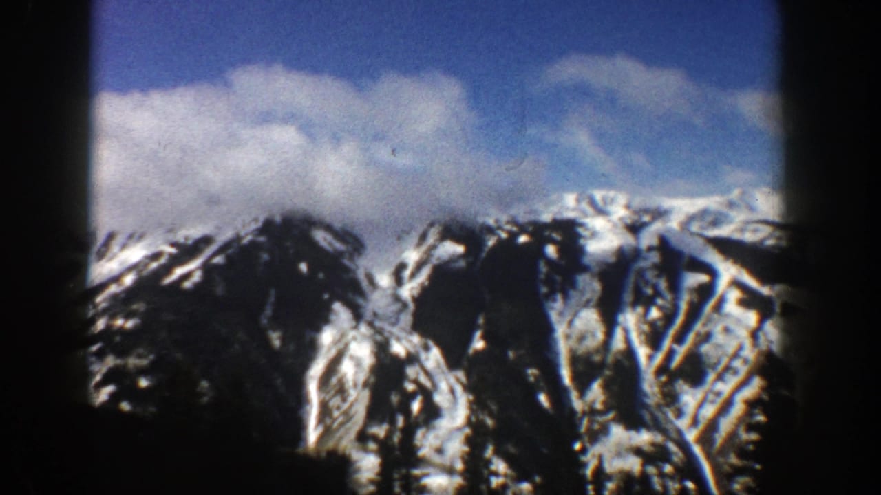 Snow-covered mountain ridges beneath blue sky and clouds, framed by dark film borders.