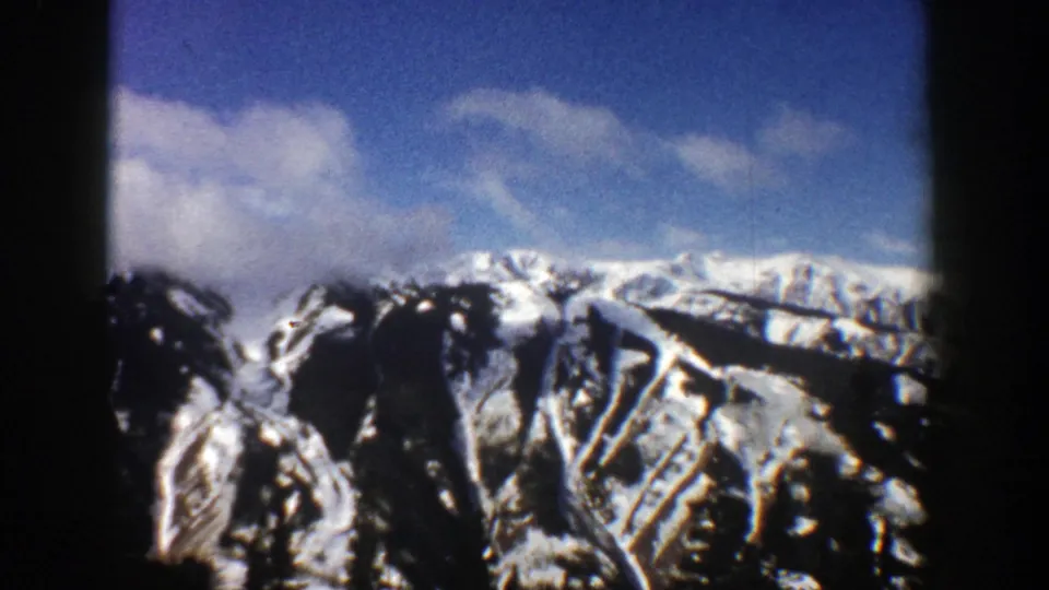 1961 Aspen, Colorado home-movie frame showing snow-streaked mountain slopes below a partly cloudy blue sky.