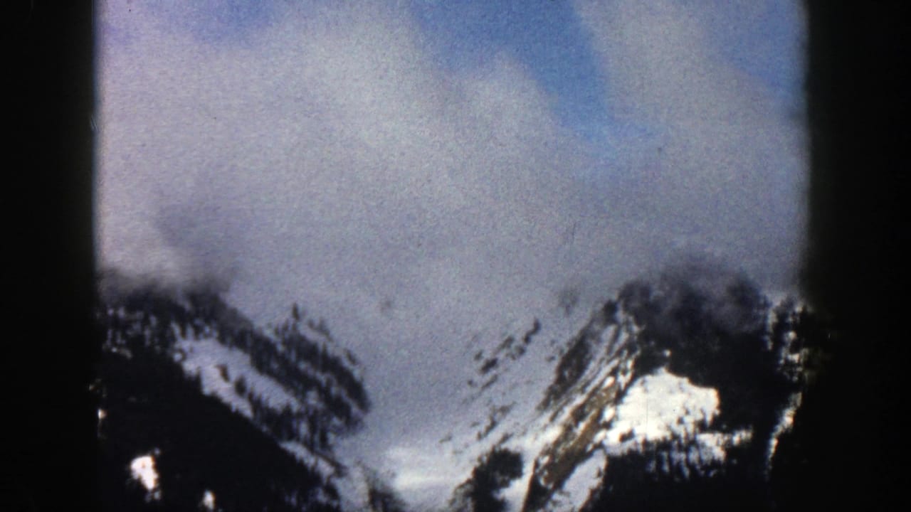 Snow-covered mountain ridges under a blue-gray cloudy sky with dark film borders.