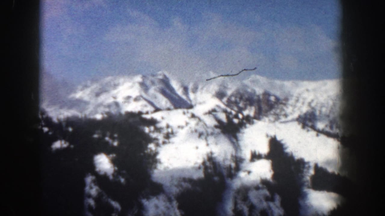 Snow-covered mountain range beneath a pale blue sky with dark foreground frame edges.