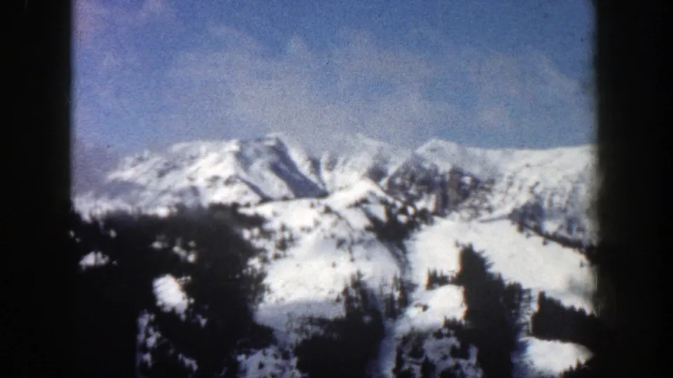 Wide 8mm view of snow-covered Aspen, Colorado mountains with dark tree-covered slopes and a clear blue sky.