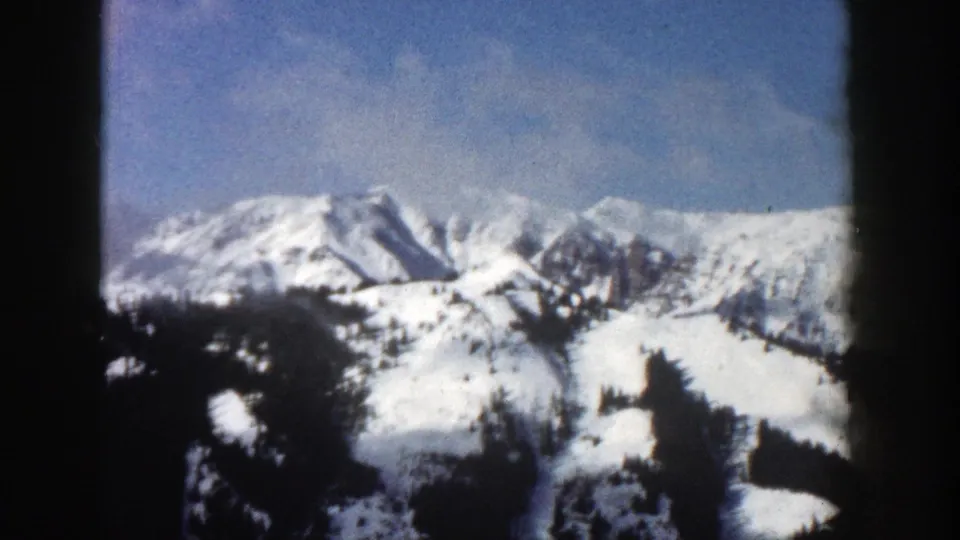 Aspen, Colorado winter landscape on 8mm film, with white mountain slopes, dark trees, and a pale blue sky.