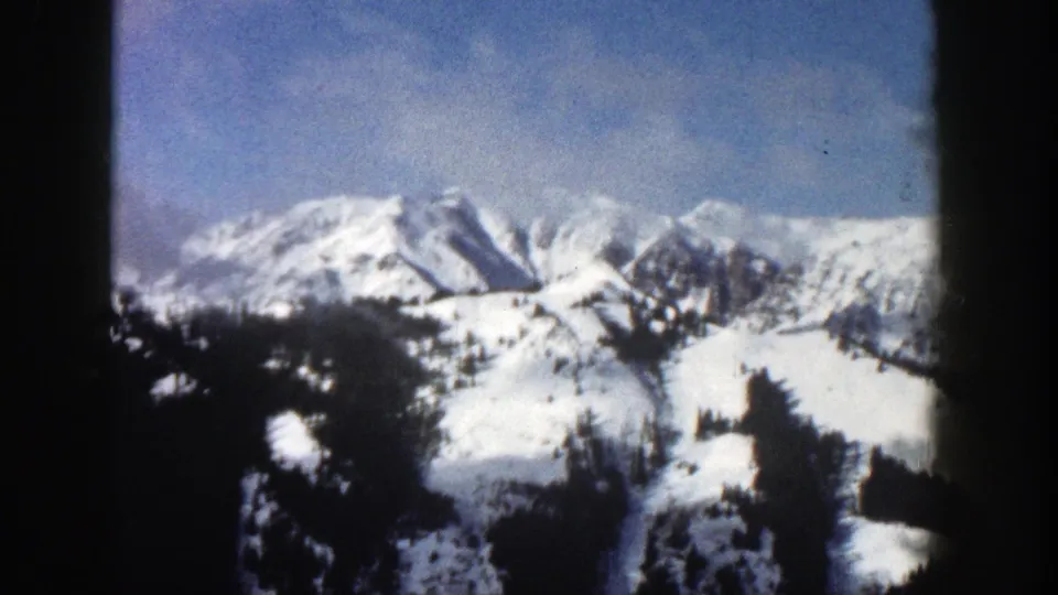 Final 1961 Aspen-area frame showing snowy mountain peaks, evergreen hills, and faint cloud in a blue winter sky.