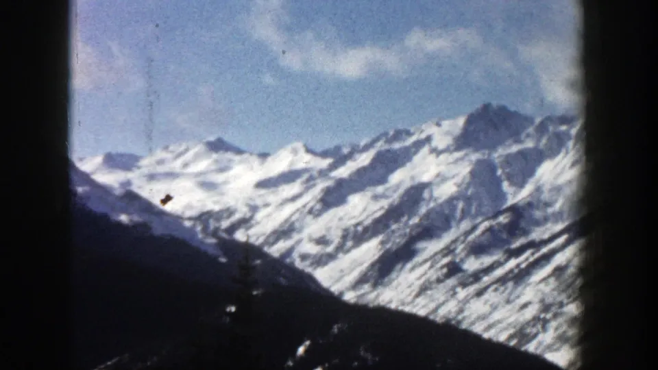 1961 Aspen, Colorado 8mm frame showing a snow-covered mountain range across a dark diagonal foreground slope.