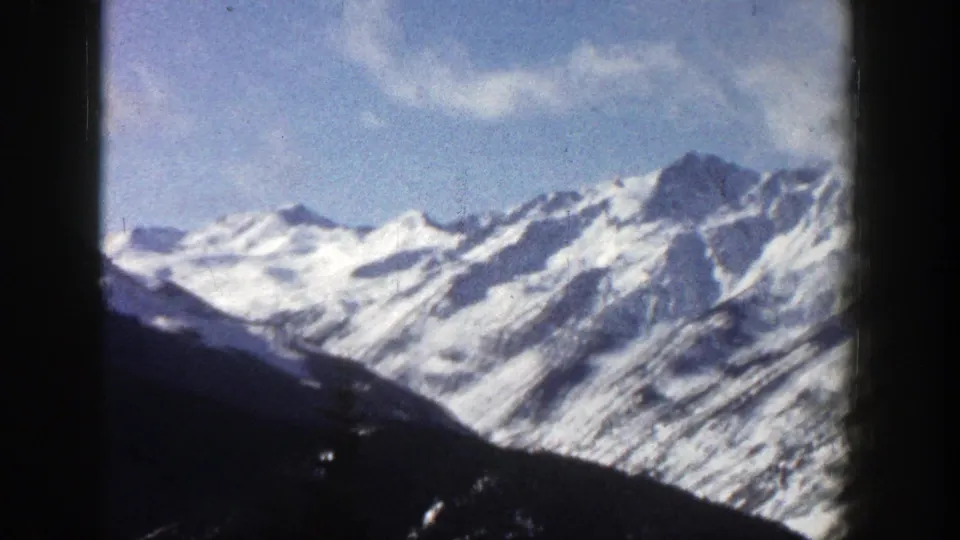 1961 Aspen, Colorado 8mm frame of bright snowy peaks and a dark foreground ridge under a lightly clouded sky.