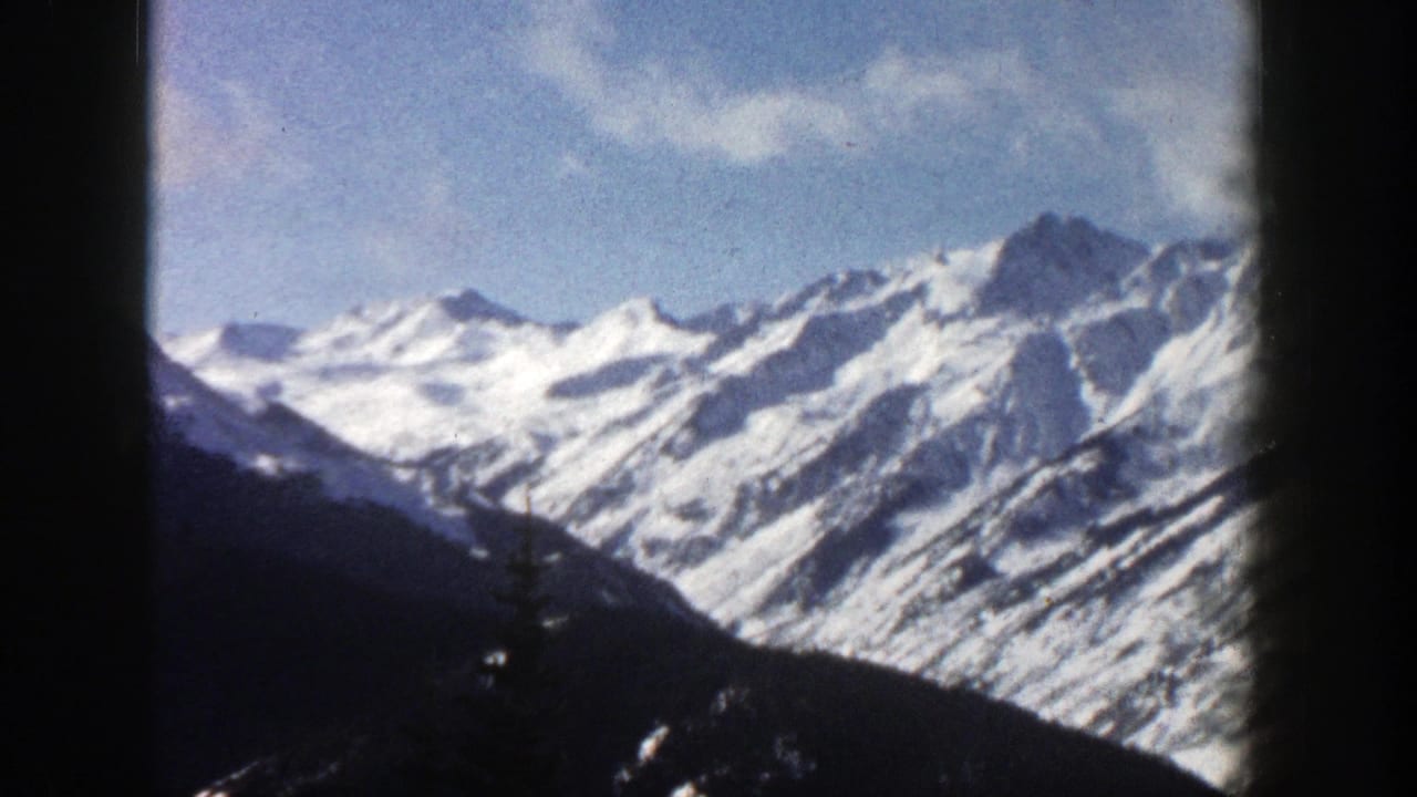 Snow-covered mountain range under blue sky with dark foreground slopes and film borders.