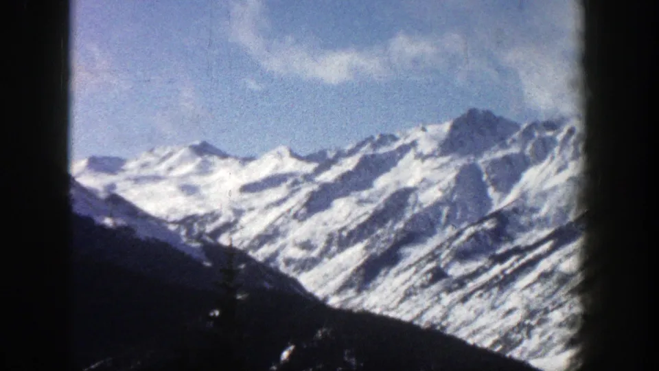 1961 Aspen, Colorado frame with bright snowy mountain peaks, rugged ridgelines, blue sky, and heavy dark 8mm border at the sides.