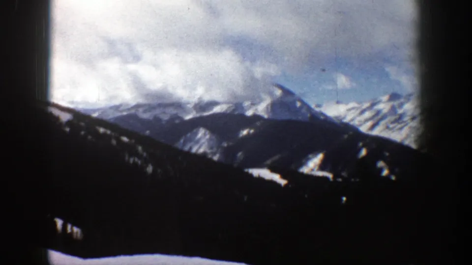 1961 Aspen, Colorado frame with a clouded alpine skyline, snow-streaked ridge, shadowed foreground slopes, and dark 8mm frame borders.