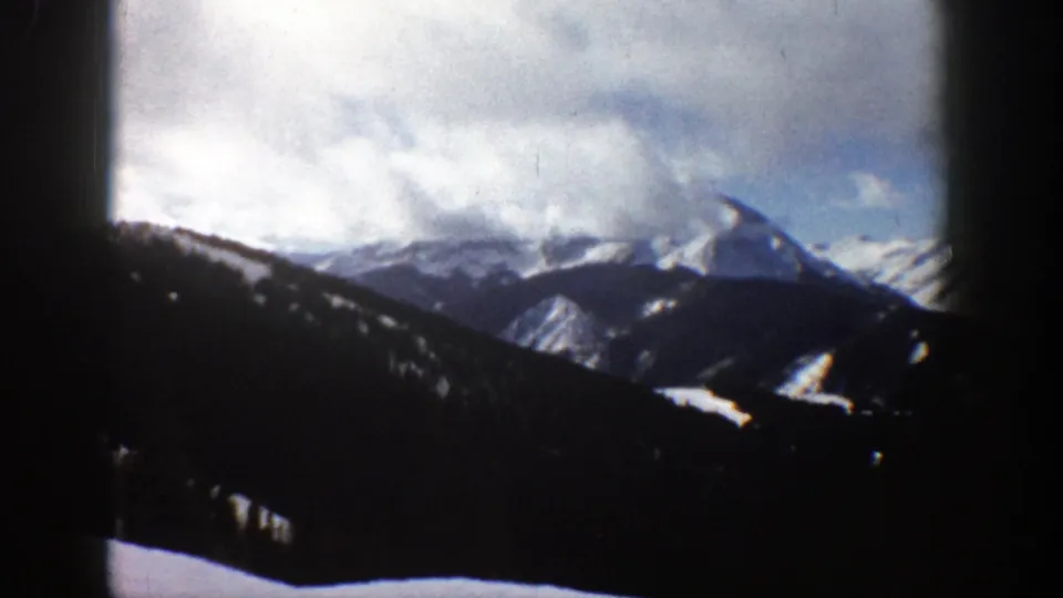 Aspen, Colorado 8mm view of distant snow-covered peaks, layered ridges, and heavy clouds in a soft vintage frame.
