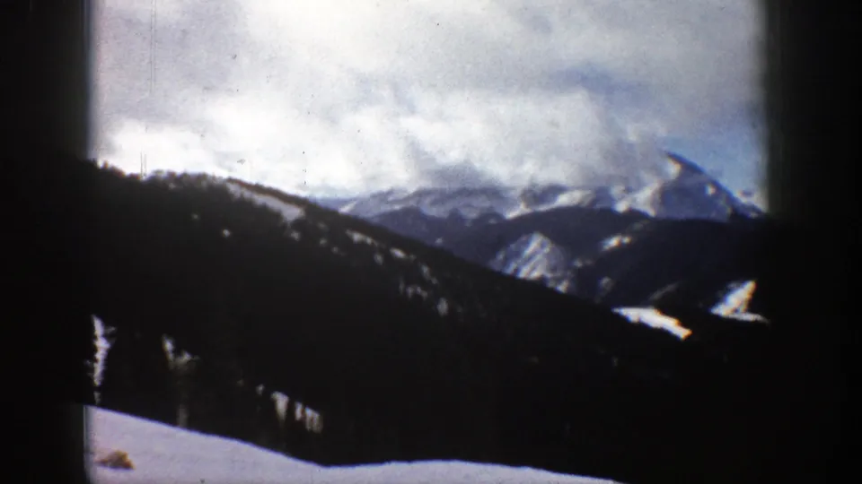 1961 8mm mountain landscape near Aspen with dark foreground hills, snow patches, and partly obscured peaks under clouds.