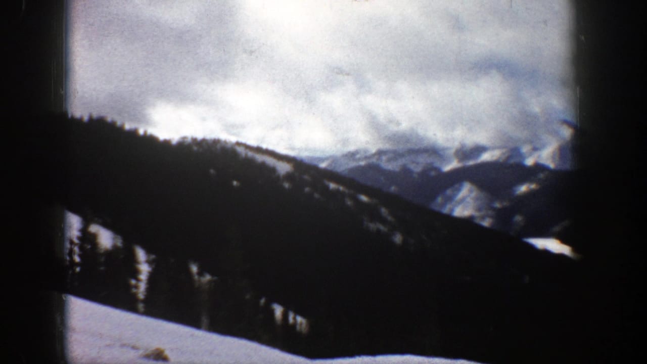 Snowy mountain slope with dark evergreen ridge and cloudy sky.