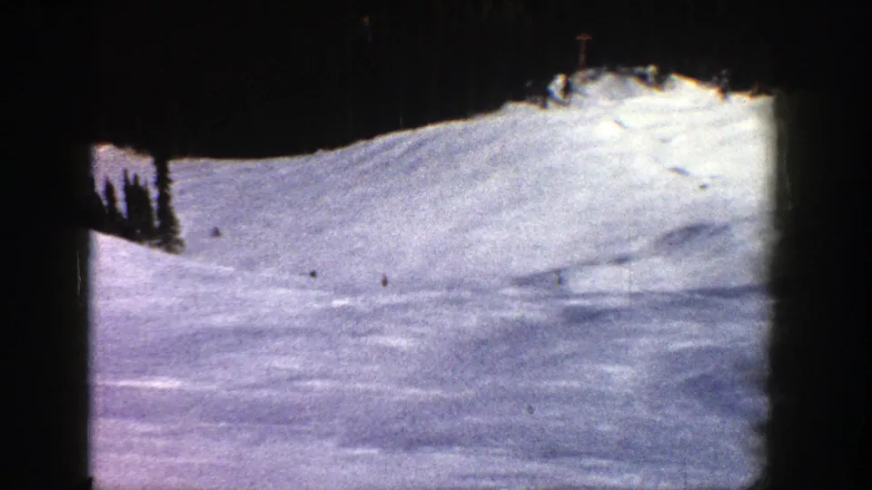 Small skiers cross a sunlit Aspen snowfield in 1961, with dark trees at the upper edge of the slope.