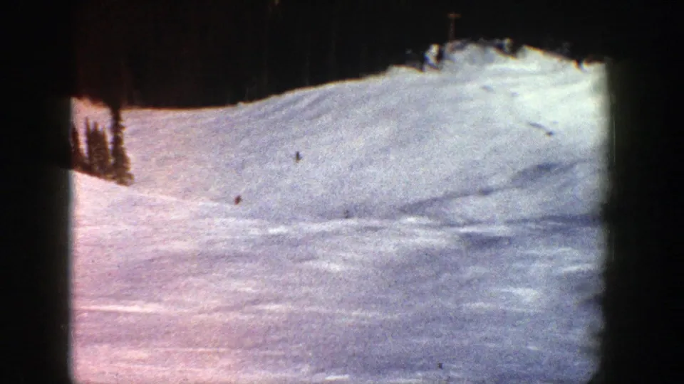 1961 Aspen ski scene with tiny figures on a wide, bright mountain slope framed by trees and 8mm film edges.