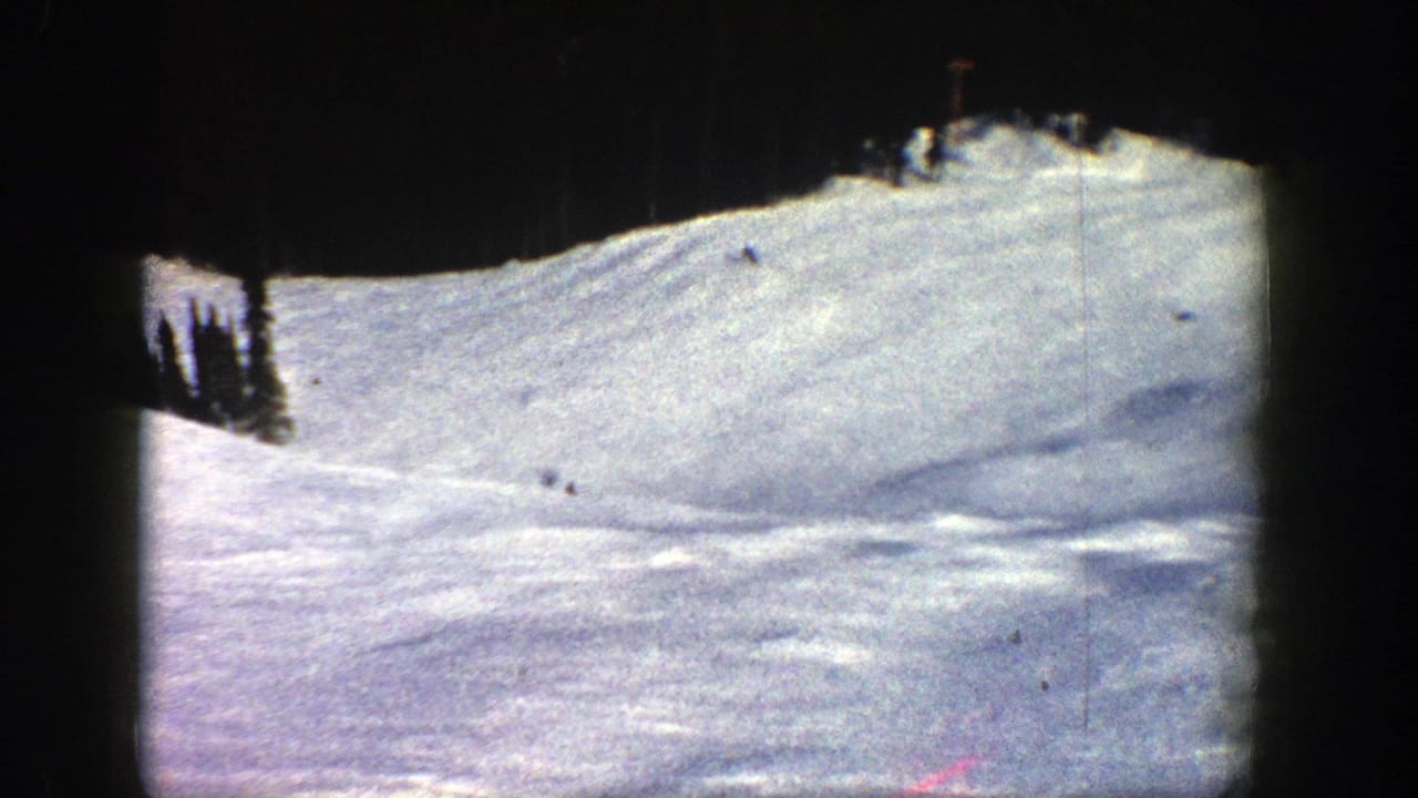 1961 8mm Aspen, Colorado frame showing a broad snow-covered ski slope with tiny skiers descending beneath dark gate-edge borders.
