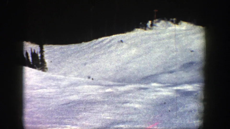 1961 8mm Aspen, Colorado frame showing a broad snow-covered ski slope with tiny skiers descending beneath dark gate-edge borders.