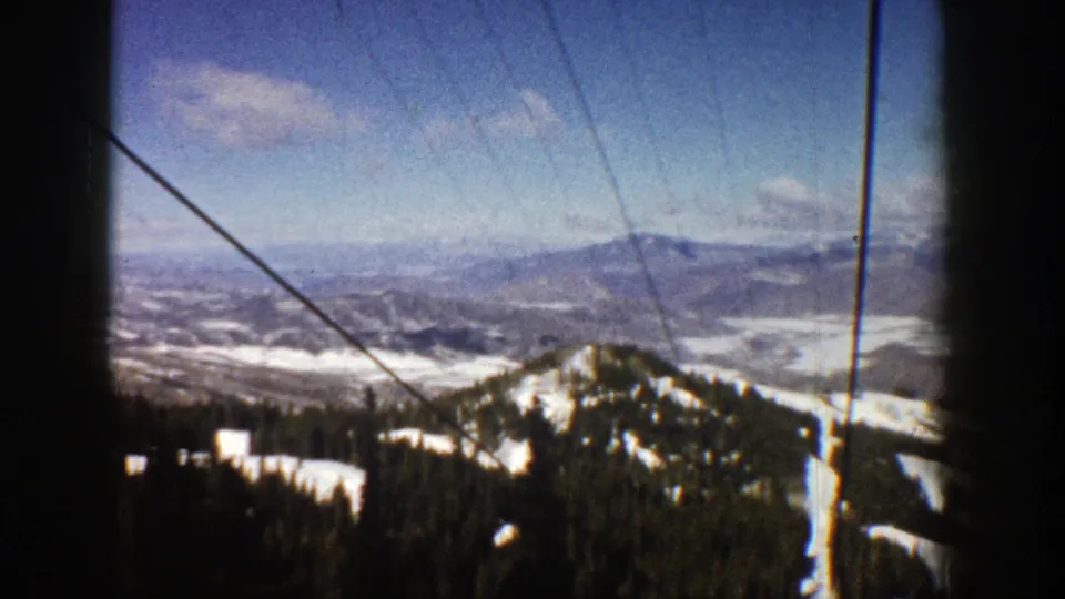 Vintage 8mm Aspen view from 1961 showing snow-bright slopes, dark evergreen forest, distant mountains, and visible cable lines.