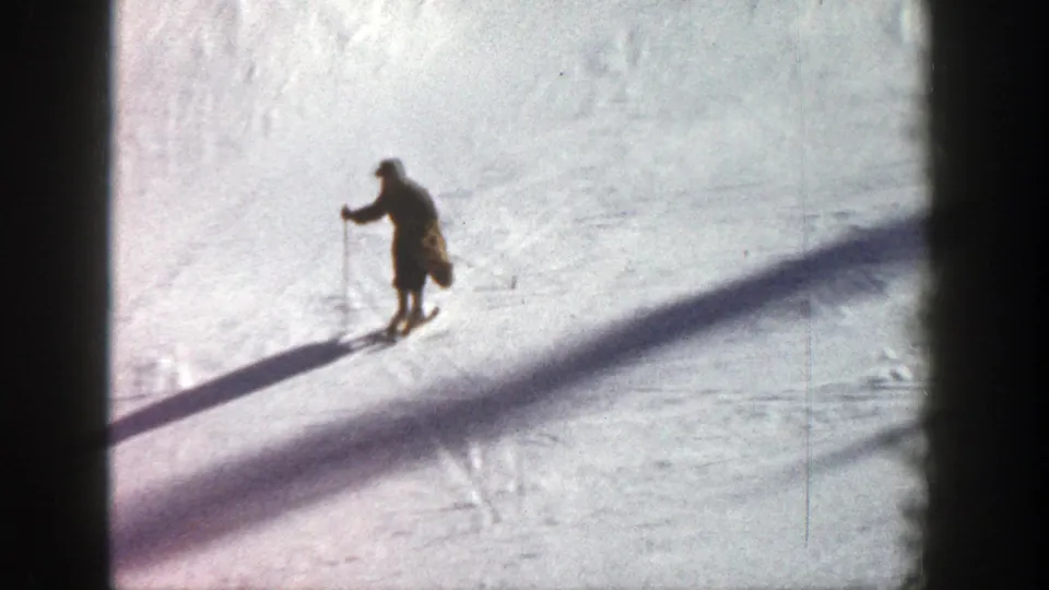 1961 Aspen home-movie frame showing a distant skier in dark clothing moving across a sunlit snowy slope.